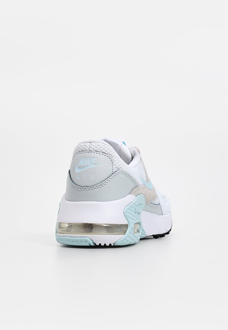 Zapatillas Nike Air con una parte superior de malla blanca y acentos de ante gris, un talón en un tono azul claro y una unidad de amortiguación de aire visible en la suela.