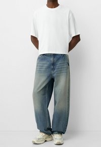 Vit, kortärmad t-shirt med croppad passform som bärs med baggy, ljusblå denimjeans med blekta områden och synliga sidofickor.