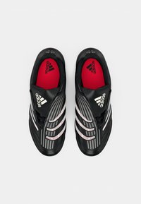 Scarpe da ginnastica nere con una finitura lucida, caratterizzate da accenti a strisce bianche e rosse, sovrapposizioni testurizzate e solette rosse con il logo Adidas.