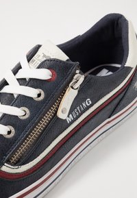 Baskets bleu marine en cuir texturé, lacets blancs et fermeture éclair latérale. Caractérisées par des bandes d'accent rouge et blanc, et le logo "MUSTANG".