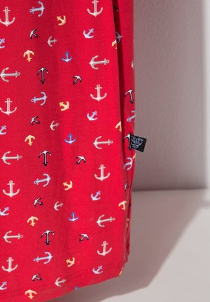 Punainen kangas, jossa on pieniä monivärisiä ankkureita valkoisina, mustina, sinisinä ja keltaisina, sekä musta vaatetunniste sivusaumassa.