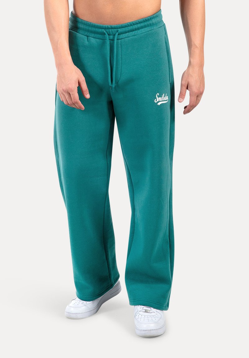 Teal joggingsbroek met een elastische tailleband en trekkoord. Bevat een witte "Smiless" logo op de linker bovenbeen. Gemaakt van een zachte, gestructureerde stof.