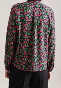 Blouse fleurie avec un fond sombre orné de fleurs roses et vertes, manches longues et coupe ample. Tissu lisse avec un léger éclat.