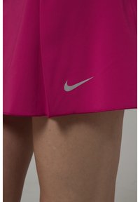 Falda deportiva rosa hecha de un tejido suave, con un logo de Nike plateado cerca del dobladillo y un diseño con abertura para facilitar el movimiento.