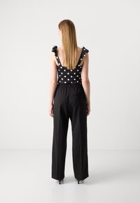 Black polka dot top with shoulder bows and black high-waisted pants, featuring a relaxed fit and side pocket detail.