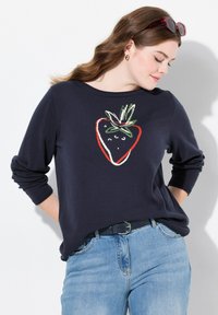Marineblauer Pullover mit einem Erdbeer-Motiv in Rot, Weiß und Grün. Hat lange Ärmel und eine lässige Passform, kombiniert mit hellblauen Jeans.