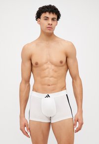 Boxers brancos para homens com uma cinta elástica preta, apresentando três riscas pretas e um suporte frontal, exibidos num modelo.