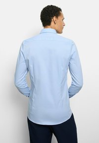 Light blue long-sleeve shirt with a pointed collar, a smooth texture, curved hem, and buttoned cuffs, shown from the back.
