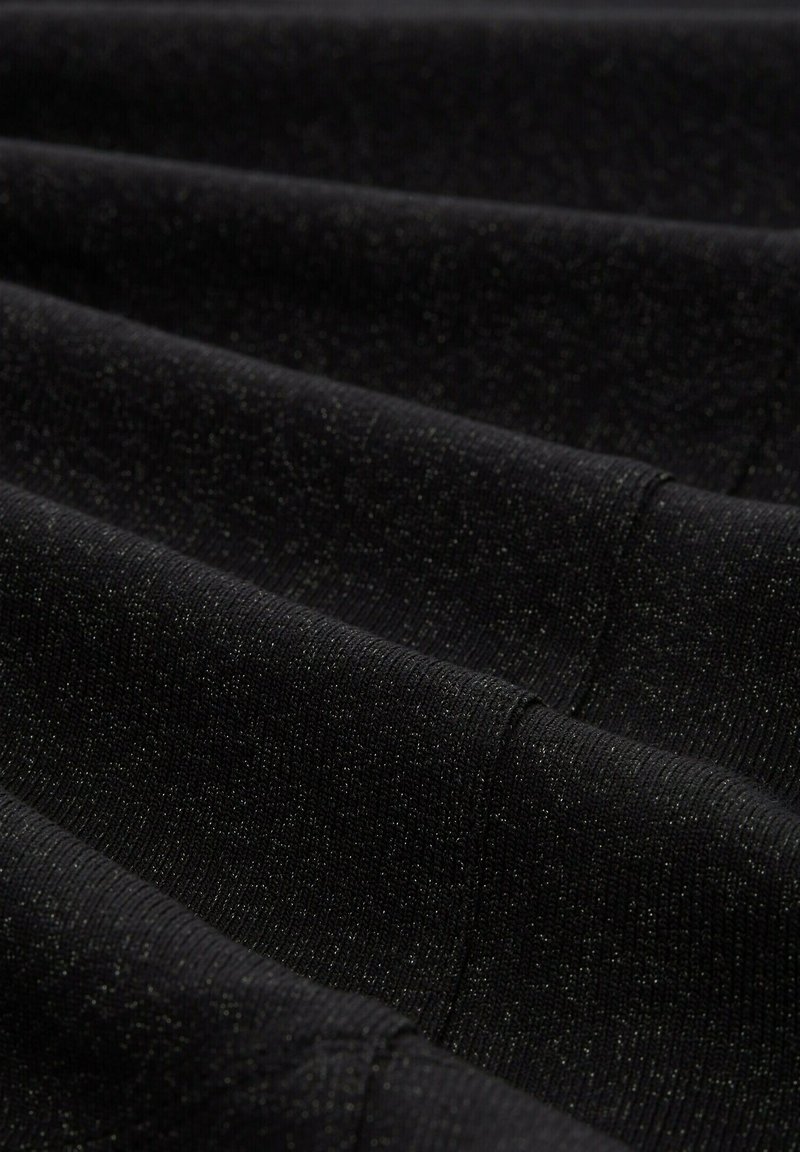 Tessuto di maglia nera con una finitura testurizzata, caratterizzato da un delicato bagliore metallico. La superficie presenta pieghe orizzontali e dettagli di cucitura.