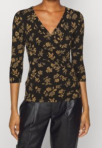 Black long-sleeve top with a V-neck and a fitted design, featuring a gold floral pattern and soft fabric texture. Paired with black leather pants.