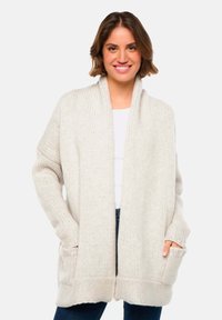 Cardigan en tricot de couleur beige clair, doté d'une texture côtelée large, d'une ouverture sur le devant et de grandes poches latérales. Manches longues et détendues.