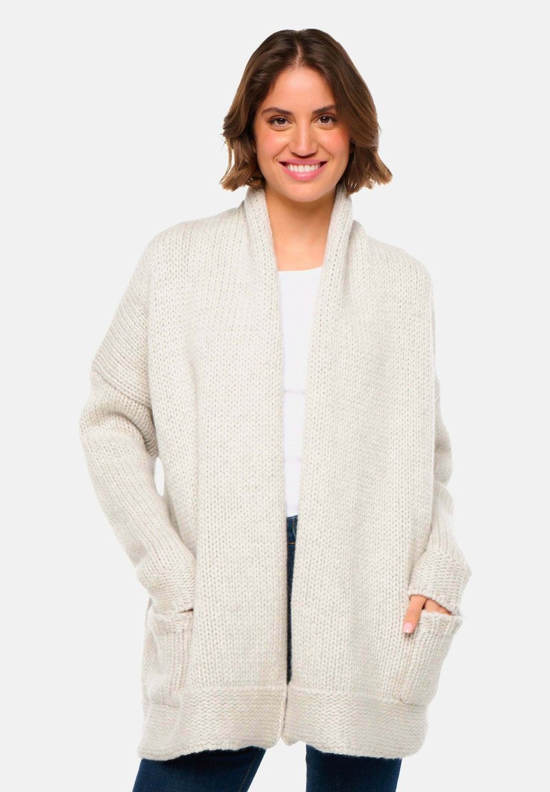 Cardigan en tricot de couleur beige clair, doté d'une texture côtelée large, d'une ouverture sur le devant et de grandes poches latérales. Manches longues et détendues.