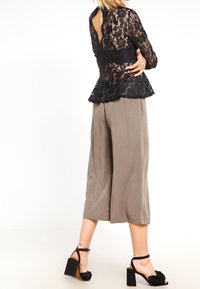 Top de peplum de encaje negro con detalle de espalda abierta, combinado con pantalones de pierna ancha gris claro y sandalias de tacón cuadrado negras.
