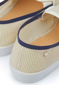 Beige geweven fabric instappers met een marineblauwe afwerking, voorzien van een gestructureerde bovenkant, geperforeerde inlegzool en een klein metallic logo detail.