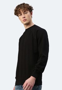 Felpa nera in cotone con scollo a girocollo, maniche raglan e polsini a coste. Texture liscia e design minimalista, esposta su uno sfondo chiaro.