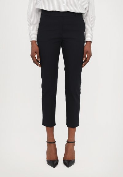 Pantalons de tailleur marine avec une coupe slim, longueur cropped et une texture lisse. Portés avec des escarpins noirs à bout pointu et une chemise rayée.