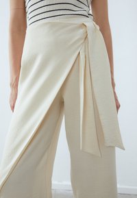Light beige wrap pants made of a soft, textured fabric, featuring a draped design and a tied accent at the waist.