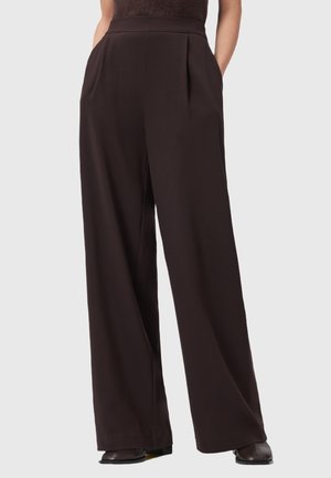Pantalons larges de couleur marron foncé en tissu lisse, avec des plis à l'avant, des poches latérales et une coupe ajustée.