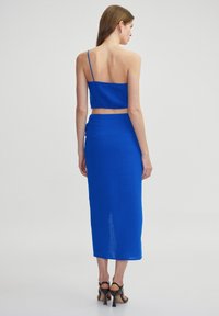Blauw twee-delige outfit met een aangesloten crop top met dunne bandjes en een lange, vloeiende rok met een zijsplit en geplooid detail.