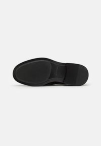Suela de zapato de goma negra con una superficie lisa y plana, bordes redondeados y un ligero tacón. Presenta un patrón de agarre texturizado para mejorar la tracción.