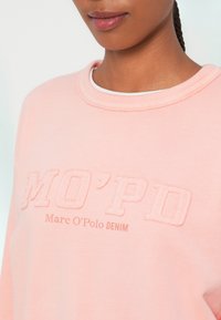 Sweatshirt rosa com decote redondo, apresentando bordado em relevo: "MO'PD" e "Marc O'Polo DENIM" em tons mais claros. Textura suave.