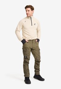 Beige fleece halvdraget topp med svarta detaljer, kombinerad med olivgröna cargobyxor med flera fickor och en svart logotypapplikation. Svarta skor.