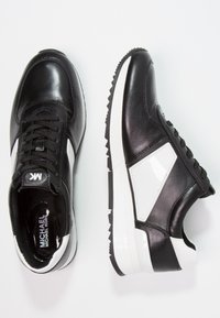 Černé kožené tenisky s bílými akcenty, vybavené texturovanou boční panelem, kulatou špičkou, šněrováním vpředu a drážkovanou gumovou podrážkou.