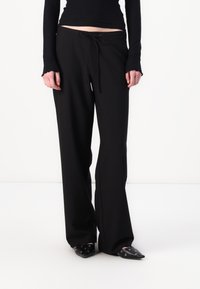 Black wide-leg pants made of soft fabric with a drawstring waist, featuring a smooth texture and subtle drape, paired with black pointed shoes.