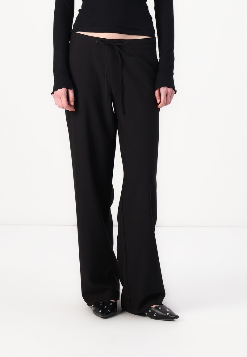 Black wide-leg pants made of soft fabric with a drawstring waist, featuring a smooth texture and subtle drape, paired with black pointed shoes.