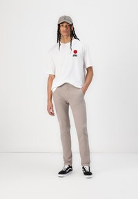 White oversized t-shirt with red circle graphic, beige tapered pants, and black sneakers with white accents; grey cap with logo.