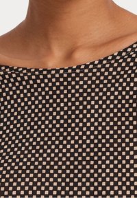 Svart- och tanfärgat mönstrat tyg med ett rutnät av små rutor; mjuk textur; bred båtringning; ribbad detalj.