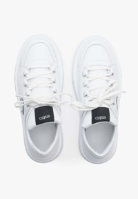 Witte sneakers met een gladde leren bovenkant, ronde neus, platte witte veters, zwart logo label op de tong en een iets verhoogde rubberen zool.