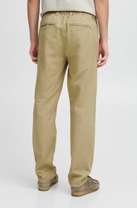 Beige, leichte Hose mit elastischem Bund, zwei Gesäßtaschen und geradem Schnitt. Der Stoff wirkt glatt und langlebig.