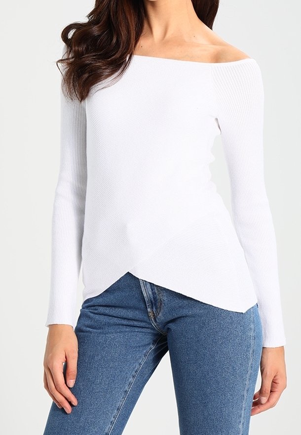 Haut blanc côtelé, à col bardot, manches longues, avec une ligne d'ourlet diagonale et une finition texturée, porté avec un jean bleu.