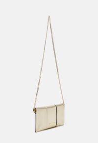 Borsa a tracolla in metallo dorato con tracolla a catena, presenta una forma rettangolare elegante, una texture liscia e un bordo nero lungo i lati.