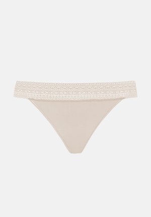 Beige thong underwear featuring a lace waistband with a scalloped edge. Smooth texture, minimalist design, and a classic cut.