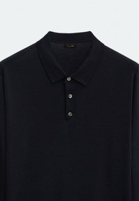Polo shirt marine en tissu tricot doux, avec un col classique, trois boutons sur la patte de boutonnage et une texture en relief.