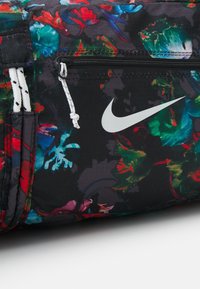 Musta kukkakuosiset Nike-tyylilaukku vetoketjupussilla, valkoisilla yksityiskohdilla ja teksturoidulla materiaalilla. Sisältää naruja ja eläviä värejä.