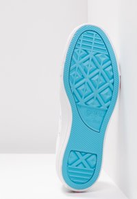 Suela blanca de zapatilla Converse All Star, que presenta una suela de goma azul con un patrón geométrico y detalle del logo, bordes superiores lisos en blanco.