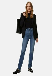 Blazer nero su una maglietta nera, abbinato a jeans in denim blu a vita alta. Una classica borsa nera e scarpe nere completano l'outfit.