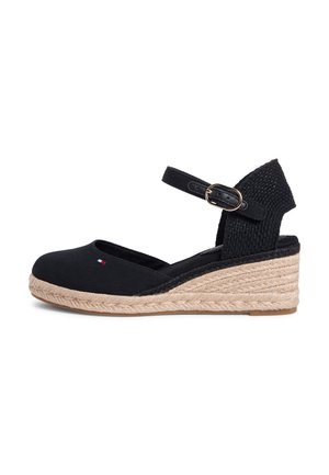 Juodi drobiniai laiveliai su pynuoto jutos platforma, čiurnos dirželiu su sagtimi ir subtiliu logotipo detalumu priekyje.