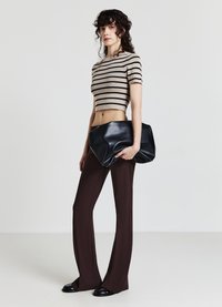 Top a coste accorciato beige e nero, abbinato a pantaloni svasati marroni. La modella tiene una grande pochette in pelle nera.