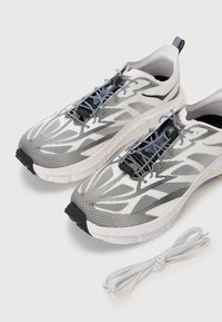 Baskets de course légères en blanc et gris avec une tige en mesh, semelle noire et un système de laçage à molette. Comprend un lacet gris séparé.