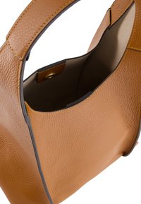 Tasche aus braunem Leder mit strukturiertem Oberflächen, geschwungenem Design und einem kontrastierend dunklen Rand. Das Innere verfügt über ein helles Futter und einen goldenen Verschluss.