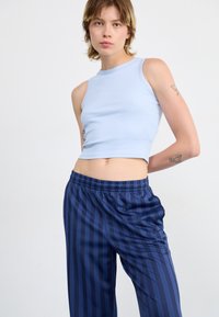 Haut crop sans manches bleu clair associé à un pantalon sombre à rayures avec taille élastique. Tissu lisse avec une silhouette ajustée et un design décontracté.