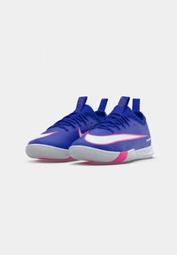 Pár modrých sportovních tenisek s bílými a růžovými Nike swooshy, tkaničkami a poutky, umístěný vedle sebe na bílém pozadí.
