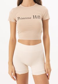 Světle béžové zkrácené tričko s textem "Primrose Hill" v černé barvě. V kombinaci s vysokými ribbed šortkami v odpovídajícím béžovém odstínu.