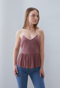 Tett, ermeløs topp i støvet rosa med V-hals og lyserosa kant, med en flagrende, plissért kant og myk stoffer.