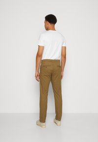 Pantaloni din bumbac maro cu croială dreaptă, cu buzunare din spate vizibile și bucle pentru curea, asortați cu un tricou alb cu mânecă scurtă.