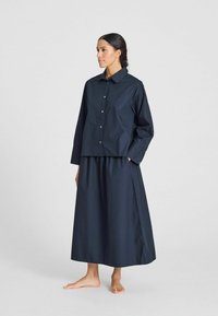 Camicia blu navy corta con bottoni e gonna lunga abbinata, realizzata in tessuto liscio con una vestibilità rilassata e un discreto dettaglio sulle cuciture laterali.